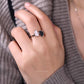 Hand wearing a silver ring with a heart design on a gray textured background
