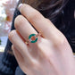 Close-up of a hand wearing a green and gold ring with a diamond.