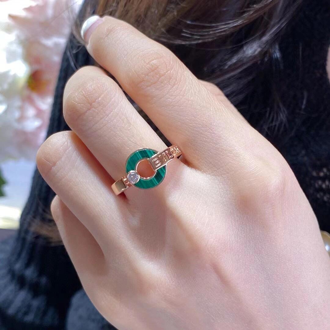 Close-up of a hand wearing a green and gold ring with a diamond.