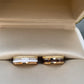 Two gold rings with white and black stones in a beige jewelry box.