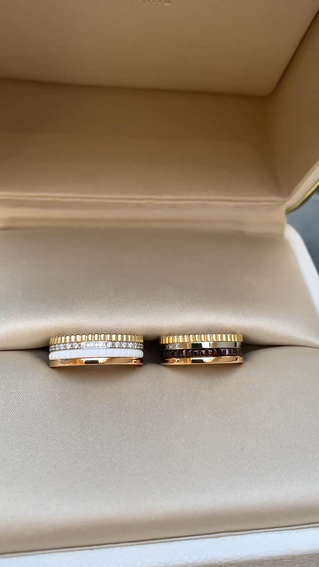 Two gold rings with white and black stones in a beige jewelry box.