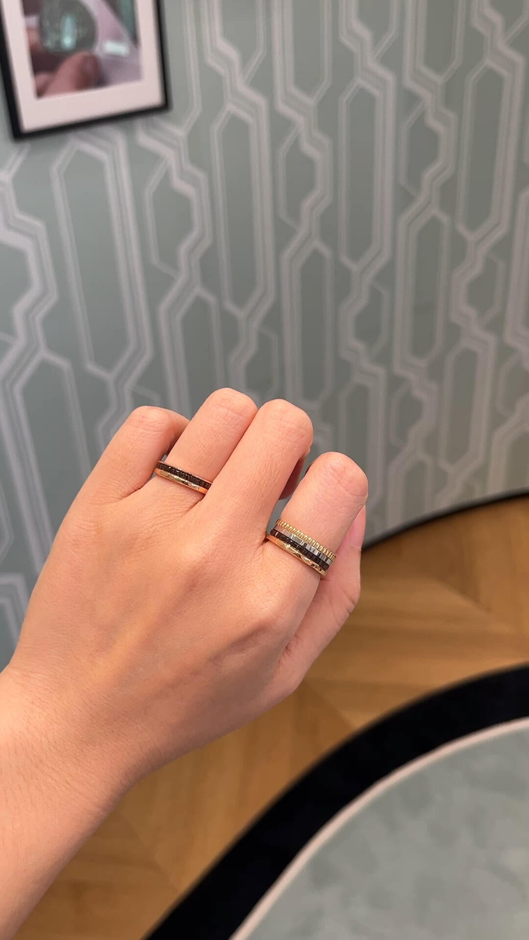 Hand wearing two rings with a patterned wall in the background