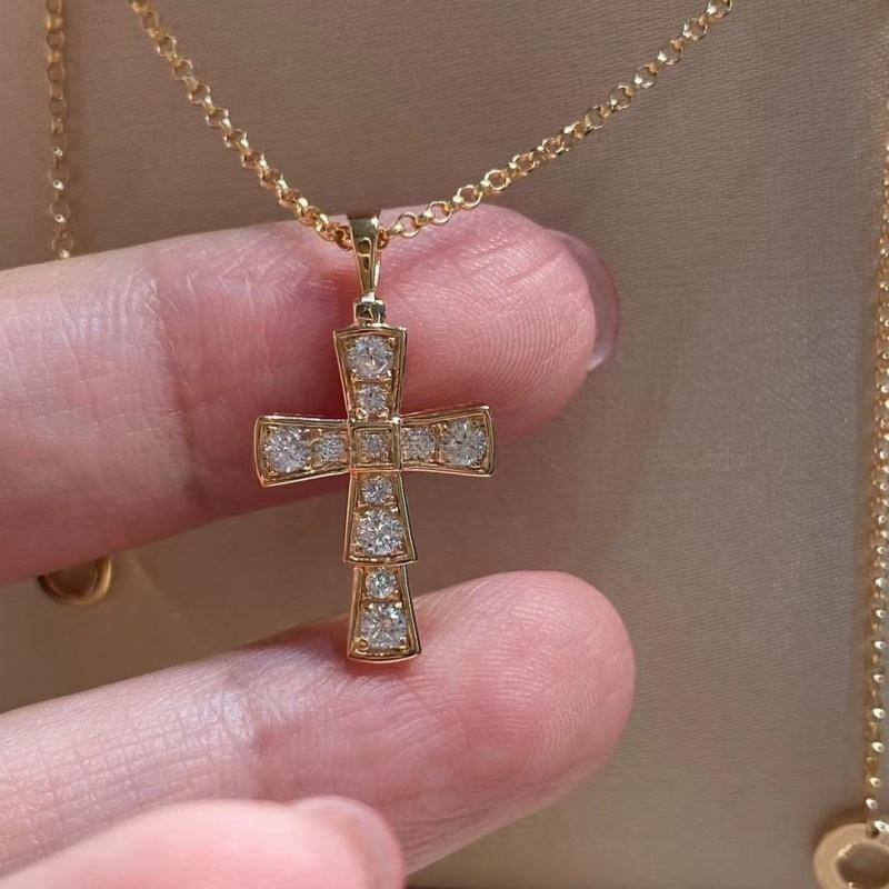 Bvlgari 18K White Gold Serpenti Cross Diamond Necklace Necklace Women Gold cross necklace with diamonds held between fingers against a beige background