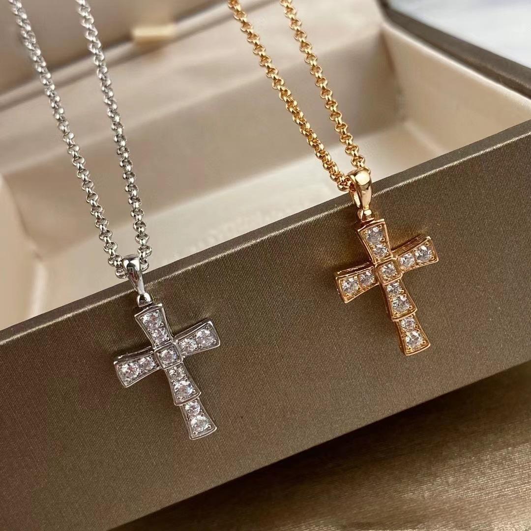 Bvlgari 18K White Gold Serpenti Cross Diamond Necklace Necklace Women Two cross-shaped pendants on chains, one silver and one gold, on a beige surface.