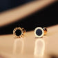 Gold earrings with black stones on a beige surface