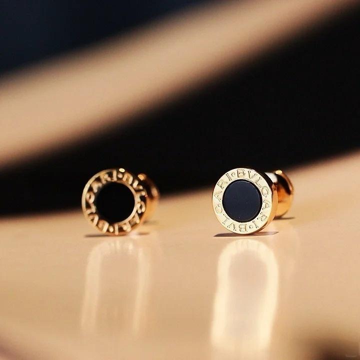 Gold earrings with black stones on a beige surface
