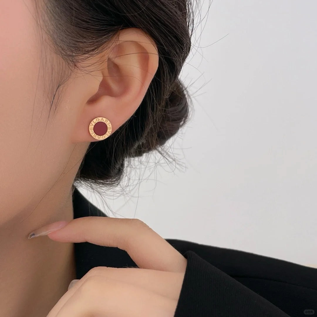 Close-up of an ear wearing a gold and red earring with a blurred background