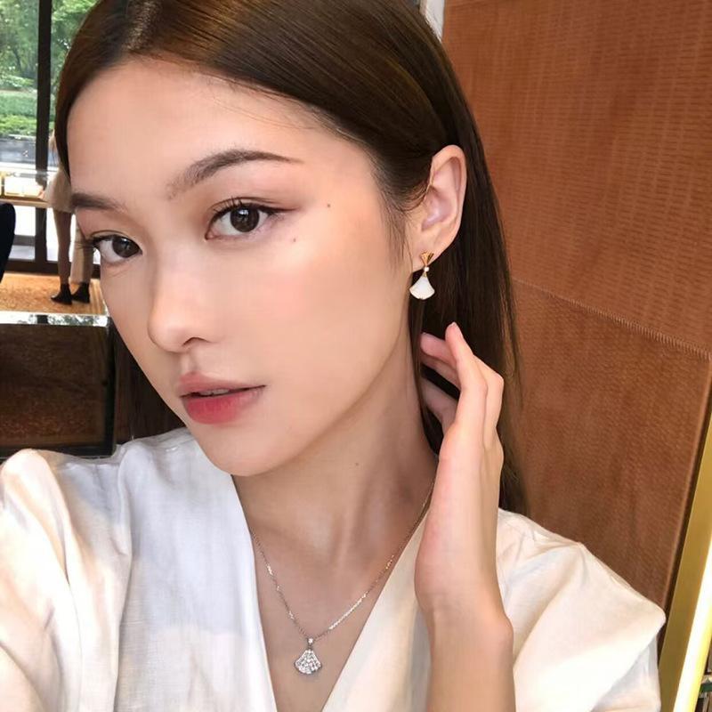 Woman wearing Bvlgari  Divas’ Dream Earrings and a necklace, indoors with blurred background