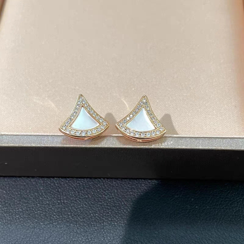 Bvlgari  Divas’ Dream Earringsand white triangle-shaped earrings on a beige surface.