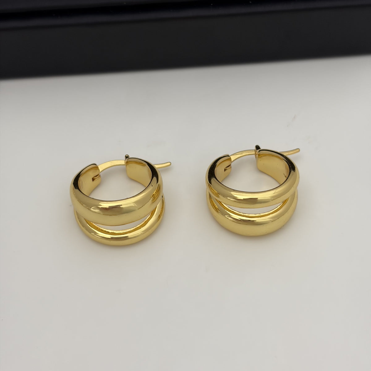 A pair of polished gold hoop earrings with a double-band twisted design, displayed on a clean white surface.