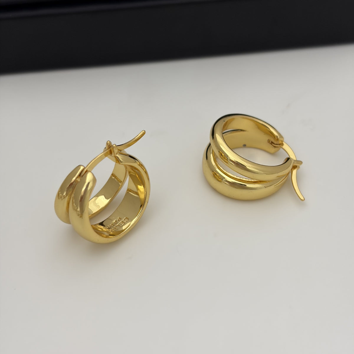 A pair of polished gold huggie hoop earrings with a triple-band design, displayed on a clean white surface.