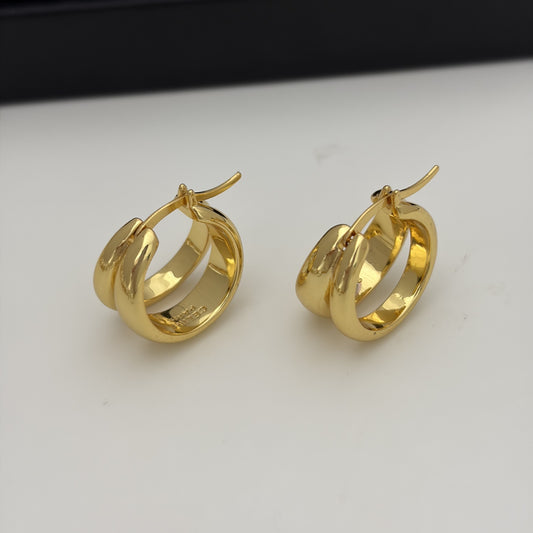 A pair of gold hoop earrings with a thick, polished double-band design and post-back closures, displayed on a white surface with a dark background.