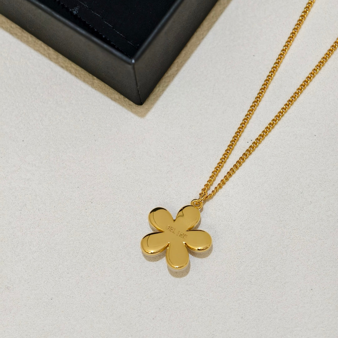 A gold-tone flower-shaped pendant necklace on a matching chain, displayed on a light textured surface next to a black jewelry box.