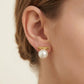 A close-up of a model's ear wearing a gold post earring with a horizontal bar engraved with 'CHIMI' and a dangling white pearl.