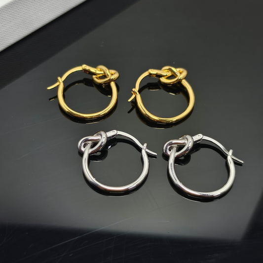 Four small hoop earrings arranged in a 2x2 grid on a glossy black surface. The top row consists of gold-toned hoops, and the bottom row consists of silver-toned hoops.