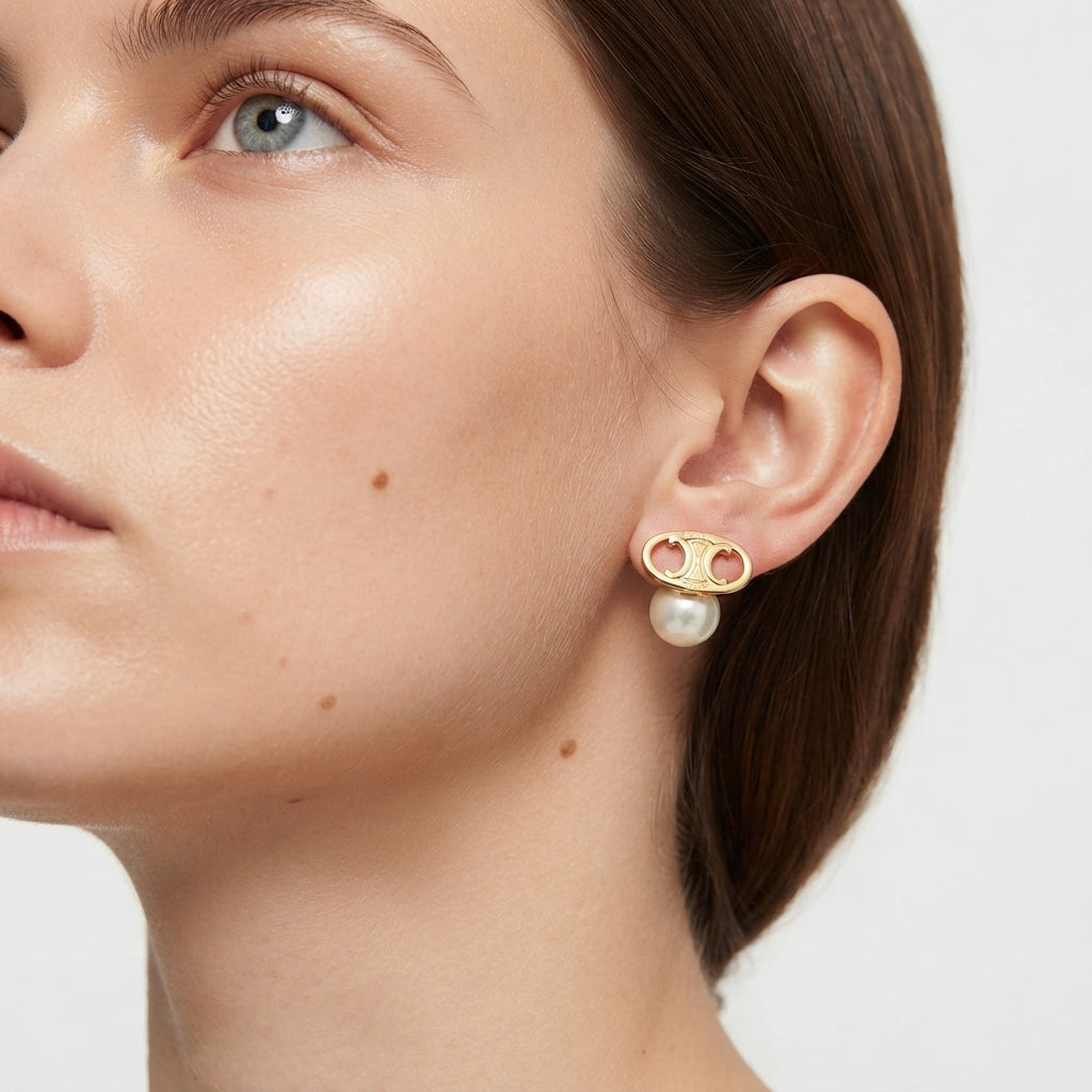 A close-up of a model's ear wearing a gold double-C logo stud earring with a white pearl drop, shown against a clean light gray background.