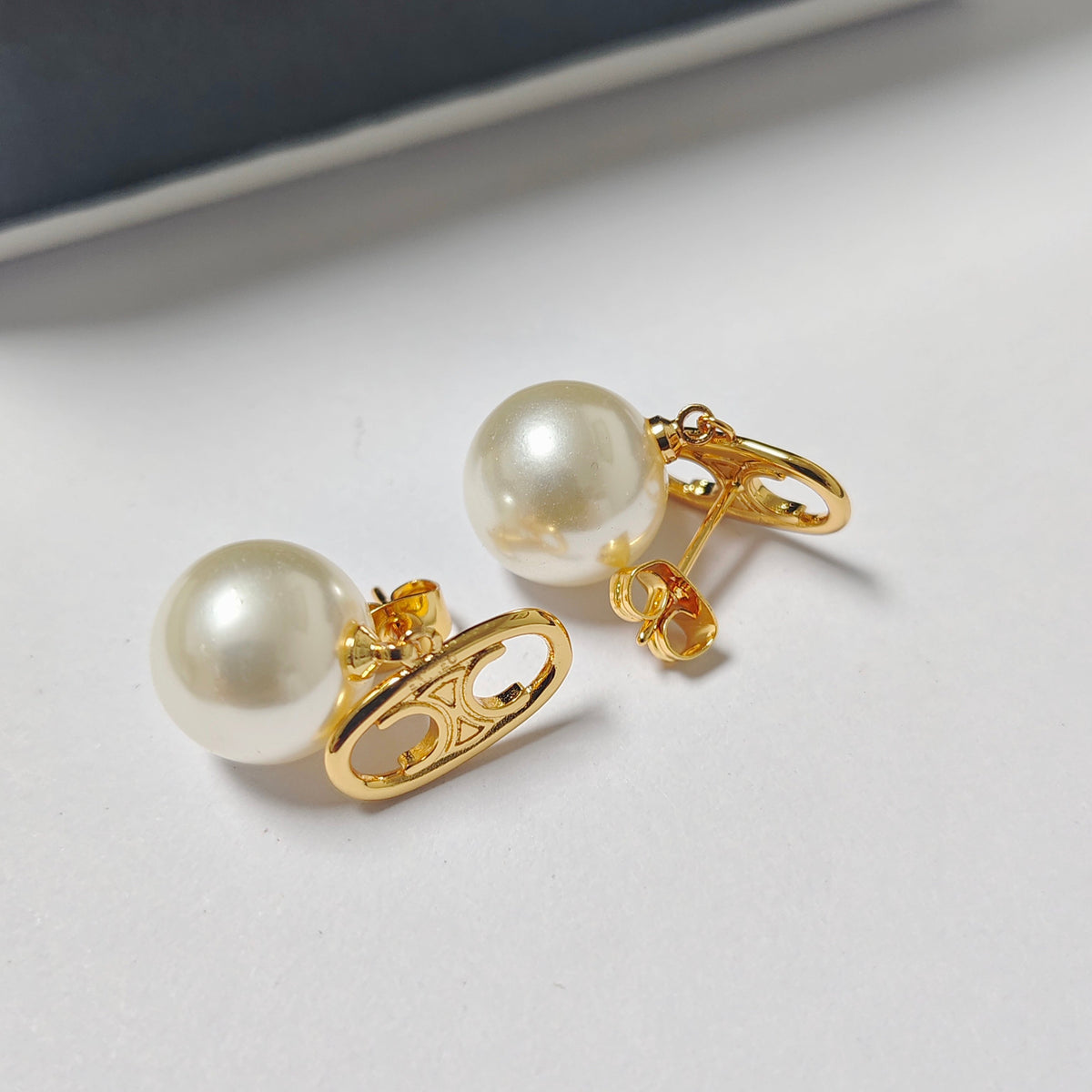 A pair of gold-toned safety-pin style stud earrings with round white faux pearls, displayed on a clean white surface.