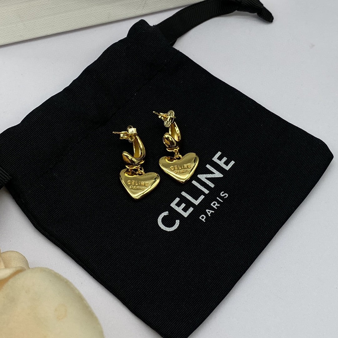 A pair of gold Celine horse and heart drop earrings displayed on a black Celine Paris drawstring pouch.