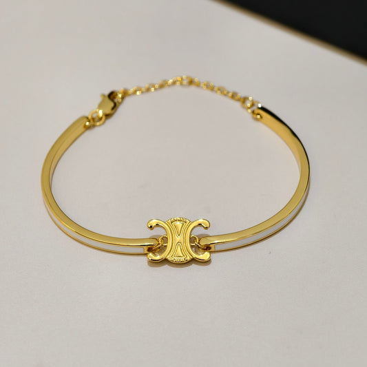 A gold-plated bangle bracelet featuring a central interlocking C logo charm, resting on a light off-white surface.