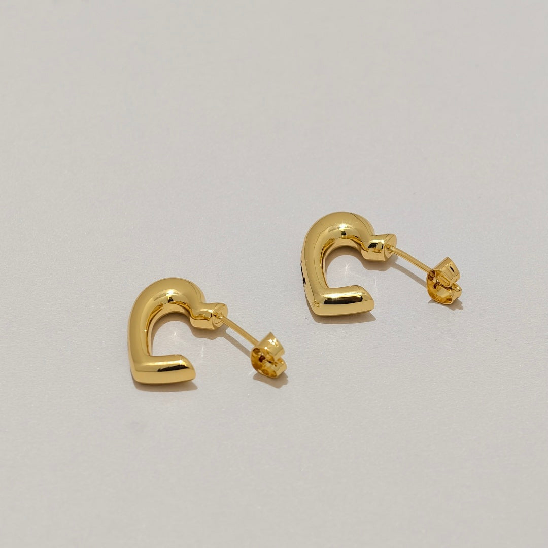 A pair of polished gold huggie hoop earrings with butterfly backings, displayed on a clean, light gray surface.