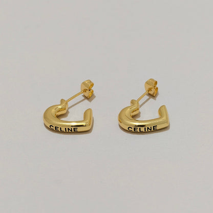 A pair of gold Celine C-shaped hoop earrings with the brand name 'CELINE' engraved in black on the front, displayed on a light gray background.