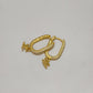 A pair of gold huggie hoop earrings adorned with small clear pavé stones and small dangling cherub charms, displayed on a neutral light gray background.