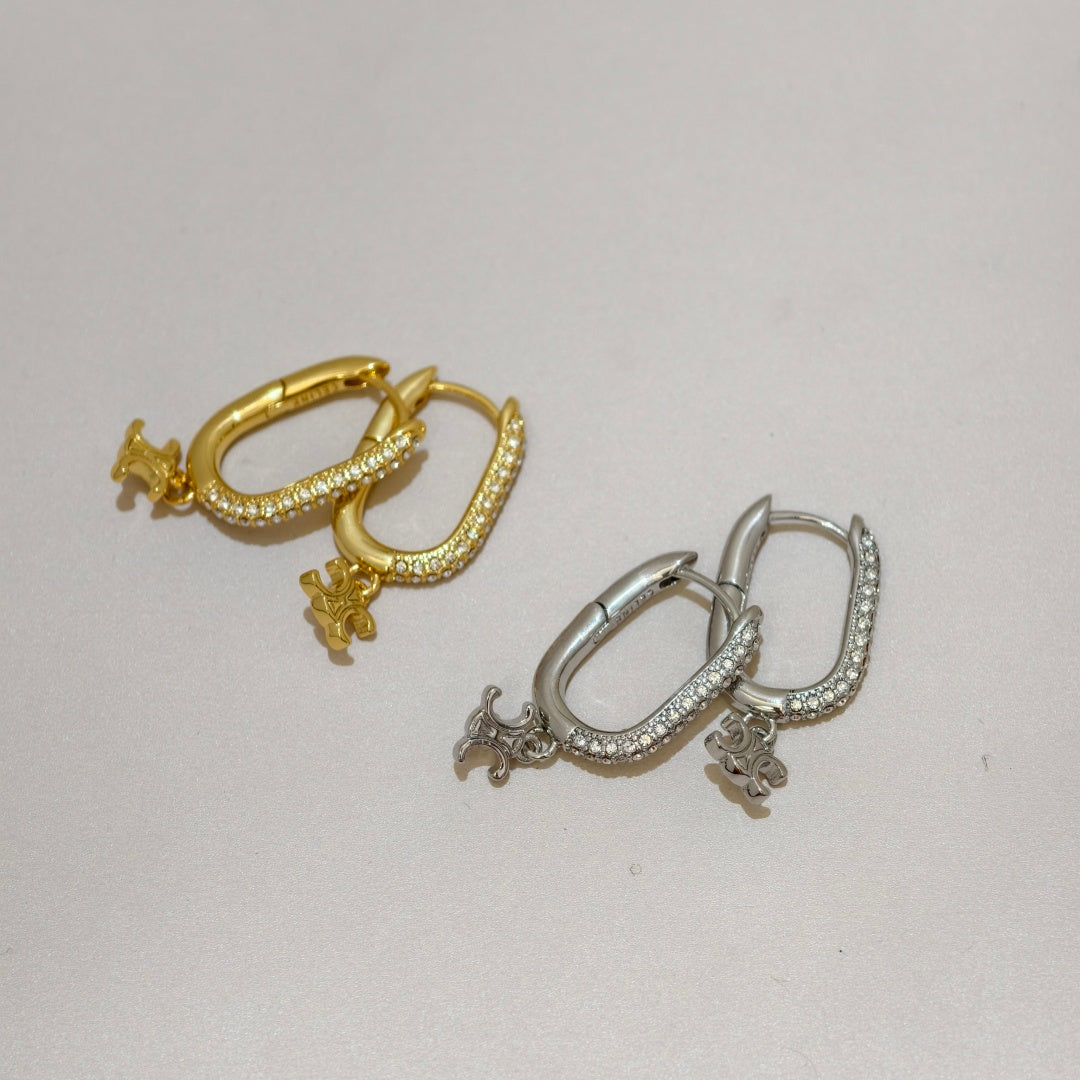 Two small hoop earrings on a plain light background, one in yellow gold and one in silver, each with a curved pavé-set band and a dangling animal charm.