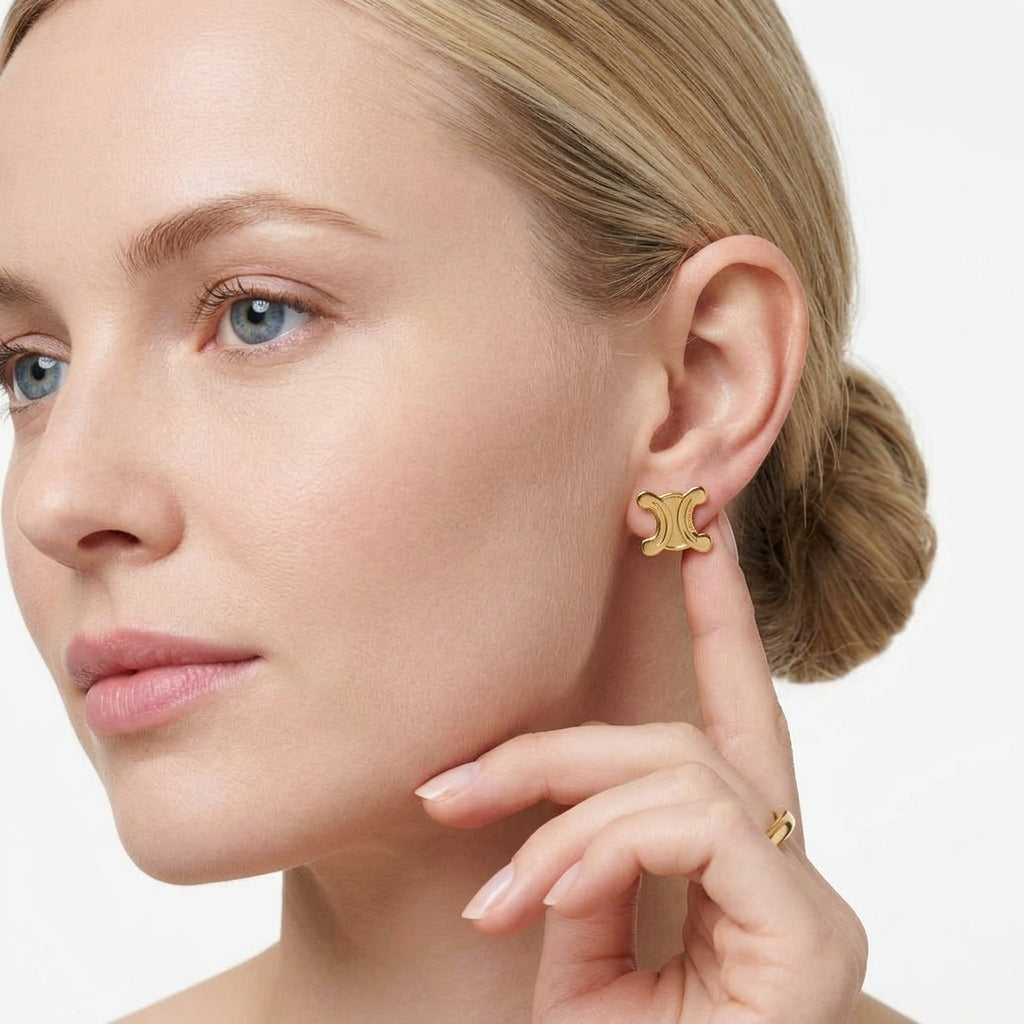 A close-up of a woman wearing a small gold earring, with her hand near her face against a clean white background.