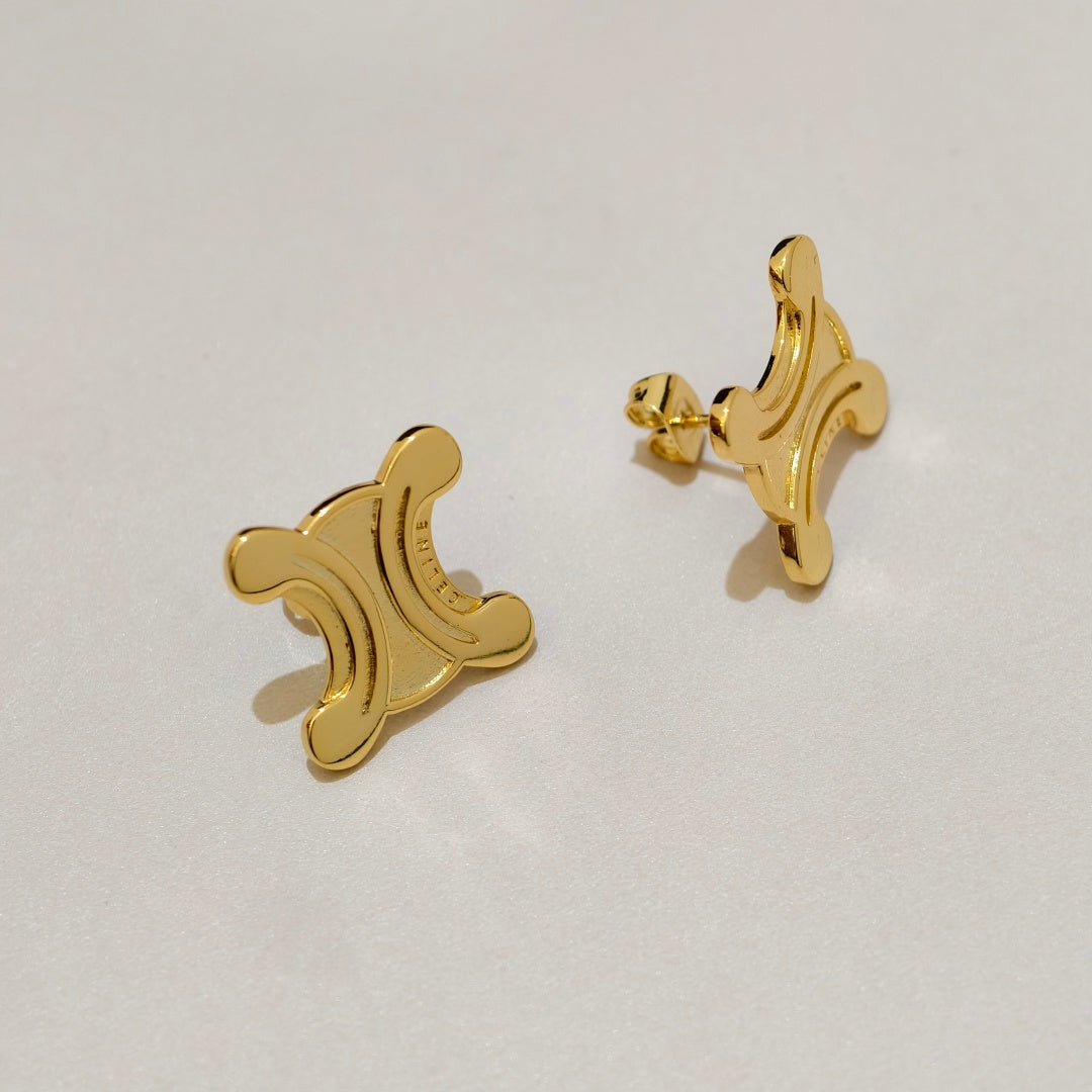 A pair of gold-tone stud earrings with an abstract, stylized crescent and loop design, displayed on a clean, light off-white surface.