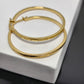 Two gold-tone hoop-style bangles with engraved 'CELINE PARIS' text, displayed on a white textured jewelry box.