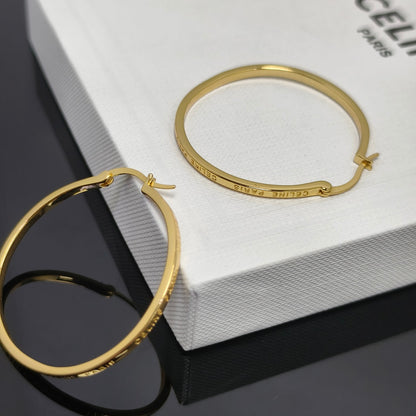 Gold hoop earrings displayed on a white textured box with the brand name CELINE PARIS partially visible, alongside a matching gold bangle bracelet.