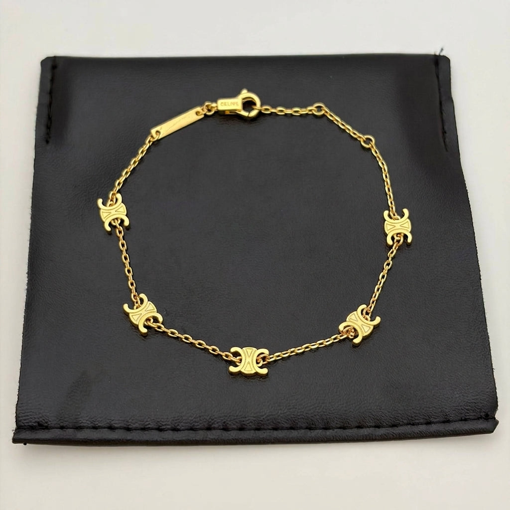 A gold-tone chain bracelet with five small Celine triomphe motifs, displayed on a black leather pouch against a light gray background.
