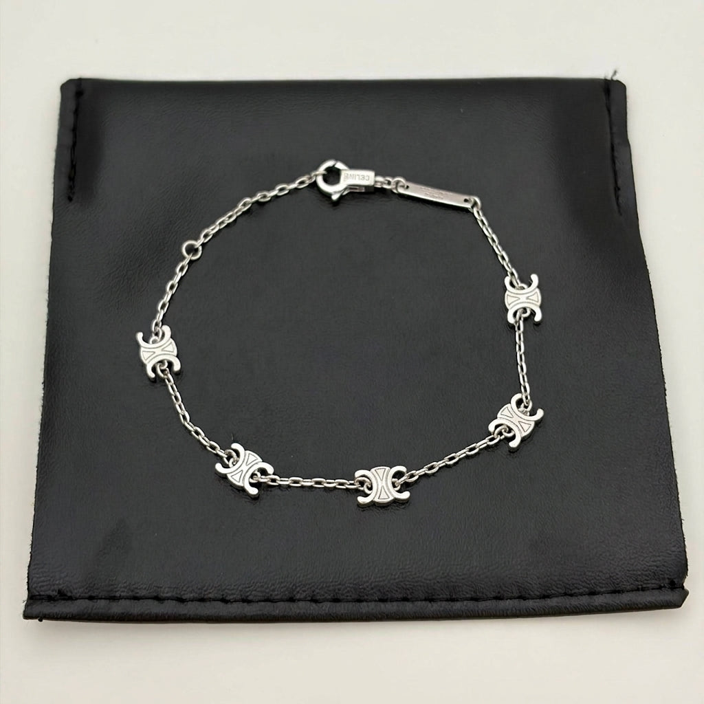 A silver chain bracelet with five small triple-C style interlocking logo charms, displayed on a black fabric jewelry pouch against a light gray background.