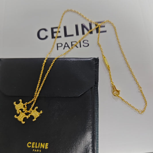 A gold-tone Celine necklace with a double-crown pendant, displayed on top of a black Celine pouch against a white background with Celine Paris branding.
