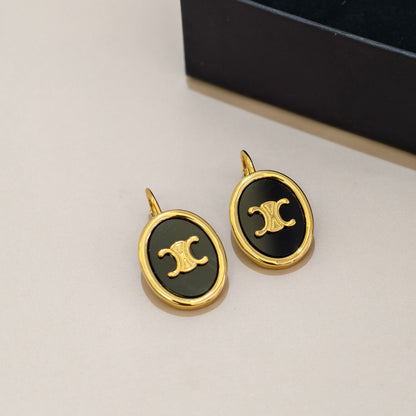 A pair of oval stud earrings with gold-tone metal frames and black enamel centers featuring a gold interlocking double-C logo, shown on a light beige surface with a dark box in the background.