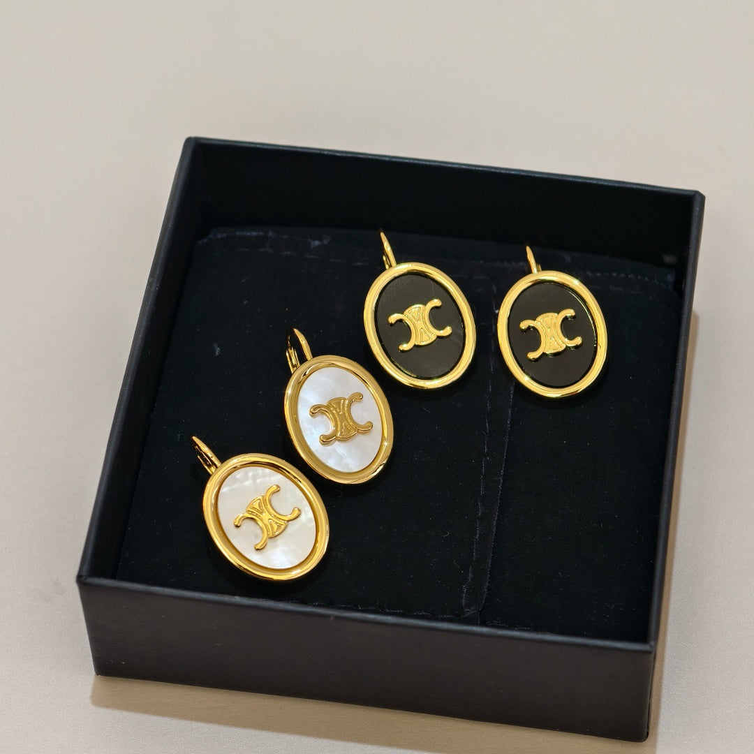 Four oval jewelry pieces with gold-tone borders and a stylized double-C logo, displayed inside a black presentation box. Two pieces have a black center and two have a white mother-of-pearl center.