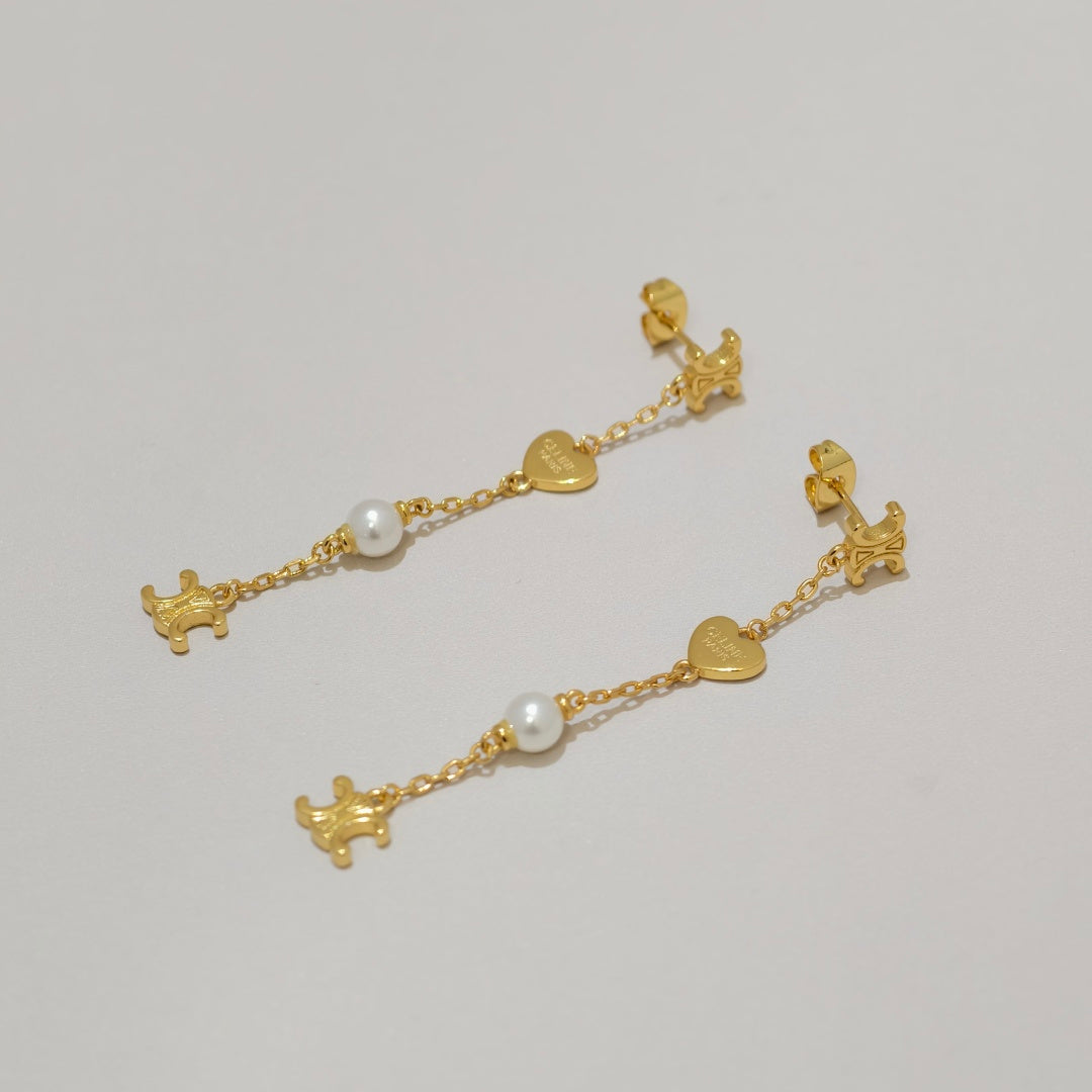 A pair of gold dangle earrings with small heart charms, white pearl beads, and tiny dog-shaped charms, displayed on a light gray background.