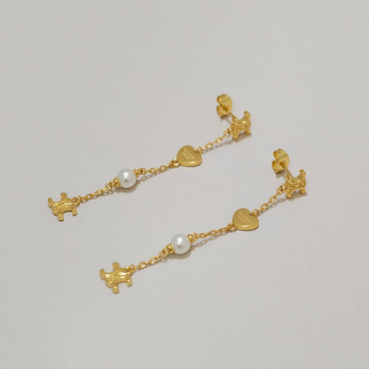 A pair of gold dangle earrings with small heart charms, white pearl beads, and tiny dog-shaped charms, displayed on a light gray background.