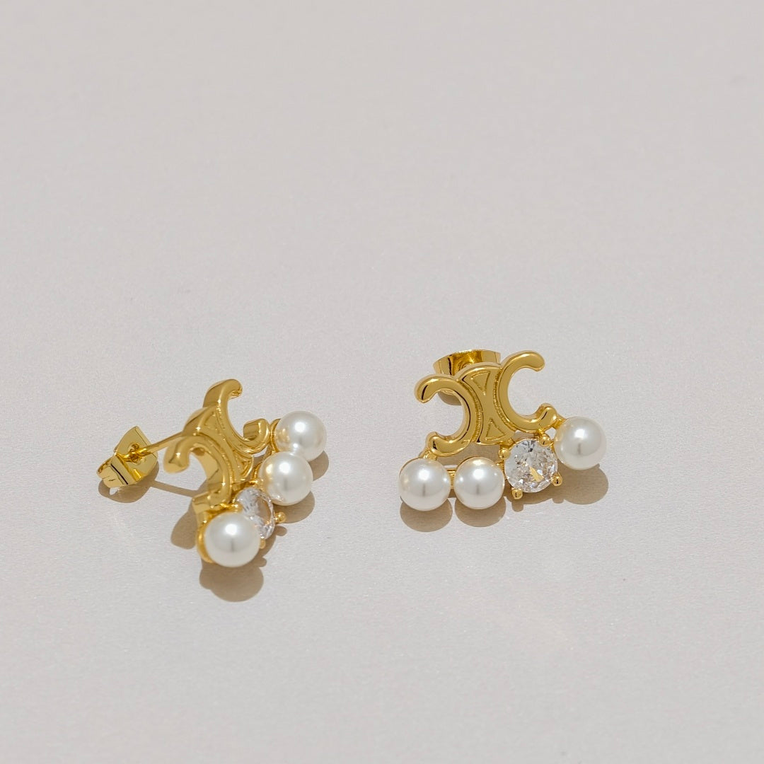 A pair of gold crescent-shaped earrings with white faux pearls and clear crystal accents, displayed on a light beige background.