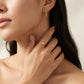 A close-up lifestyle shot of a model wearing a delicate gold ring with a small circular cutout on her finger, alongside a matching gold bar earring.