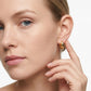 A close-up of a woman's face and ear wearing a small gold hoop earring, with her hand near her neck against a clean white background.