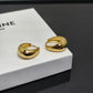 A pair of gold hoop earrings with a chunky, organic curved shape, resting on a white textured Celine box. The brand name 'CELINE' is engraved on the side of the earrings, and 'PARIS' is partially visible on the box.
