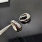 A polished silver huggie hoop earring with a teardrop-shaped front, held by metal tweezers in the foreground, with the matching earring resting in the background on a glossy black surface. The front of the earring is engraved with the brand name 'CELINE'.
