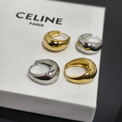 Four Celine huggie hoop earrings in polished gold and silver finishes, arranged on a white textured Celine Paris box.