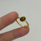 A gold ring with an oval tiger's eye stone held between two fingers against a plain light gray background.
