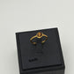 A gold ring with a round brown cabochon gemstone, displayed on a black jewelry box stand against a light gray background.