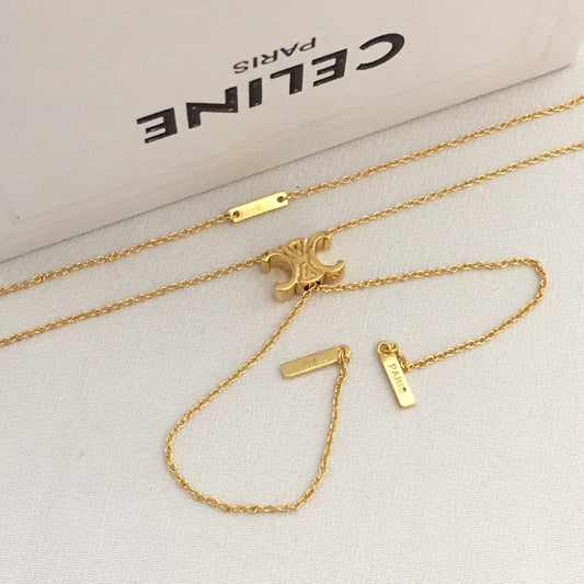 A gold-tone Celine necklace set with a signature triple-C logo pendant, displayed on a textured light gray surface with the white Celine box in the background.