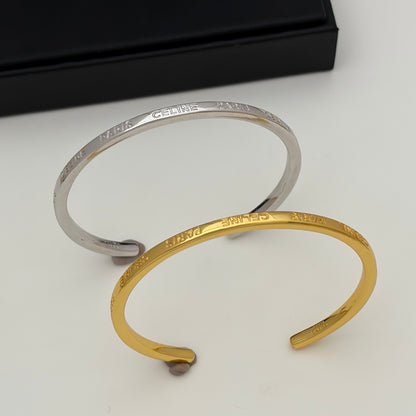 Two open cuff bracelets, one silver-toned and one gold-toned, both engraved with the name 'MARA', displayed on a light surface with a black box in the background.
