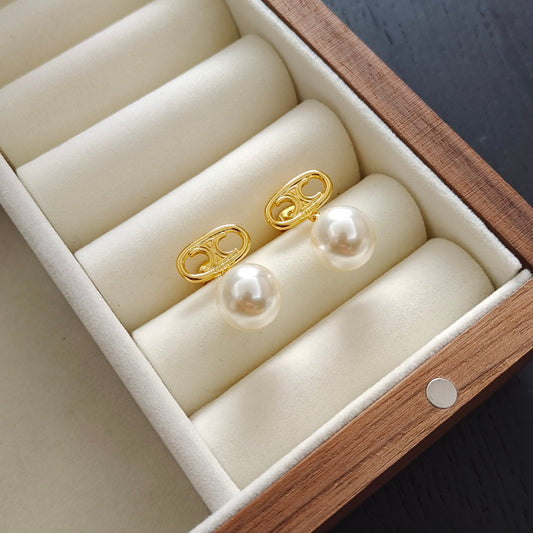 A pair of gold post earrings with round white pearls, displayed on cream-colored velvet jewelry rolls inside a wooden box.