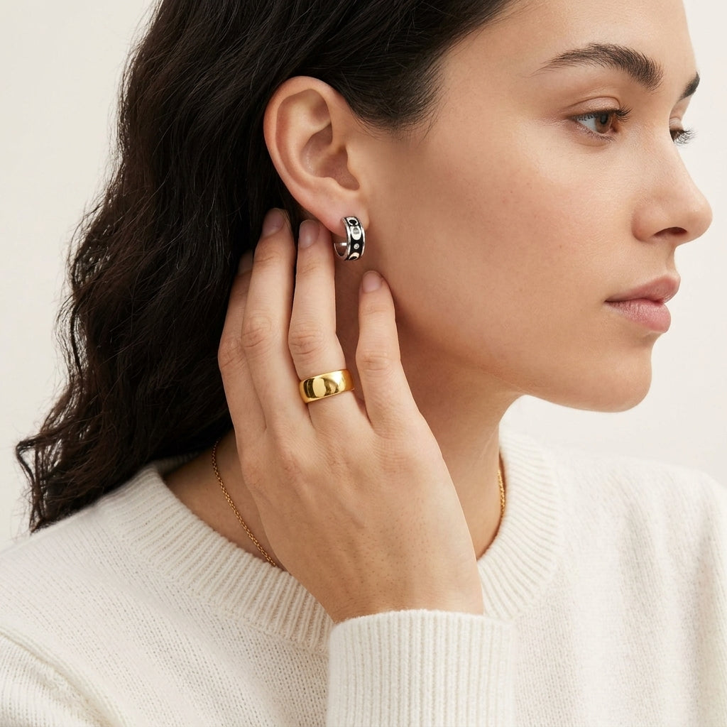 A close-up lifestyle shot of a woman wearing a small gold hoop earring and a gold ring, shown in profile against a clean off-white background.